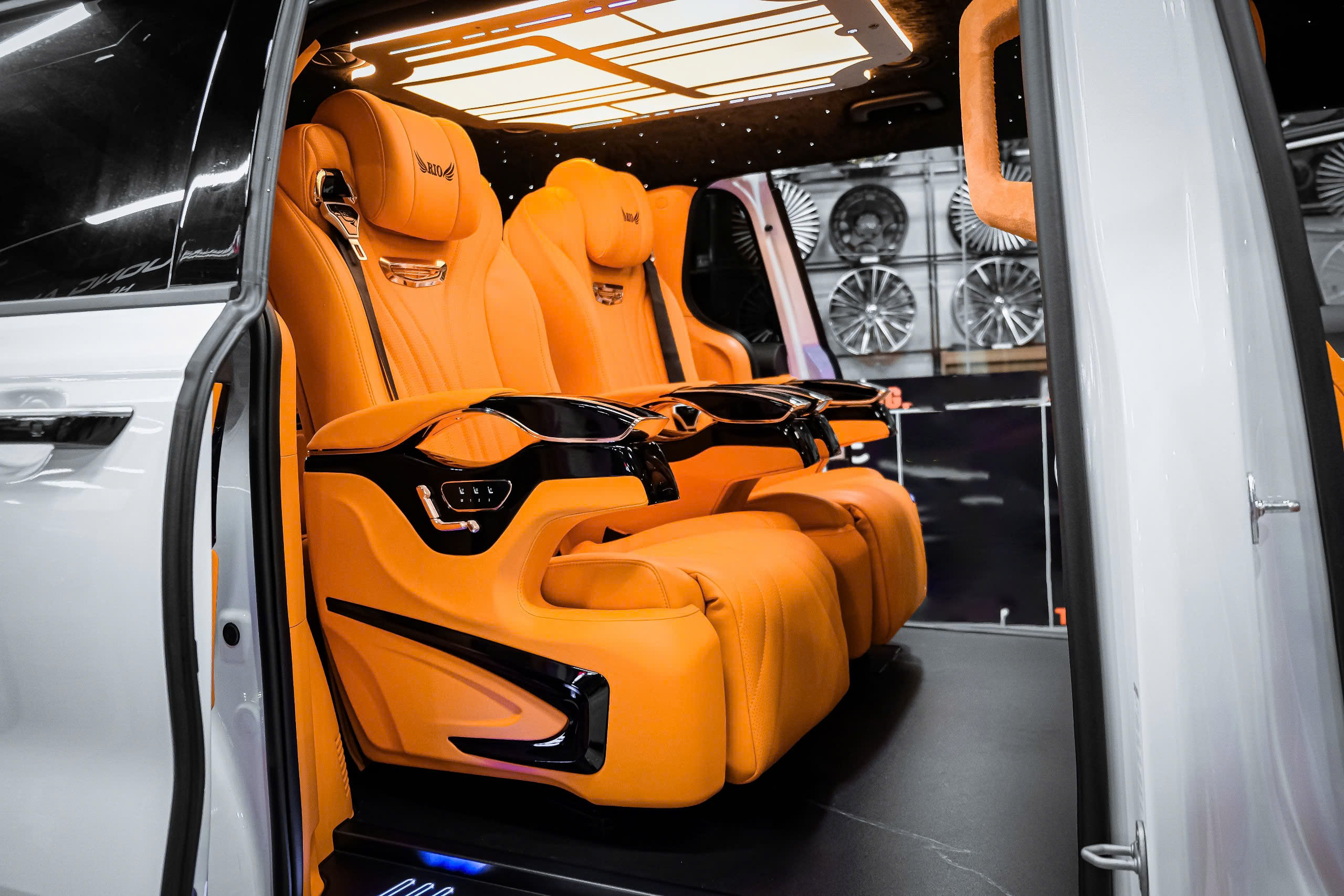 Custom Carnival cabin with orange individual seats, armrest controls and a lit ceiling panel, viewed through the open side door
