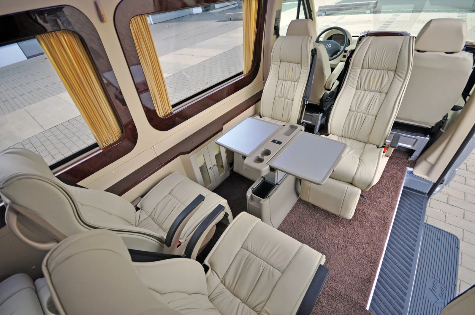 Interior of a luxury shuttle van with cream leather reclining seats, a folding table and gold curtains