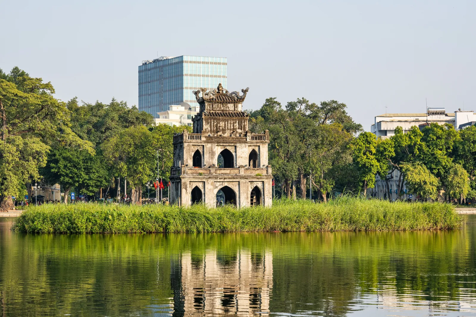 Turtle Tower (Thap Rua) on its reed-covered islet in Hoan Kiem Lake, Hanoi, reflected in calm green water